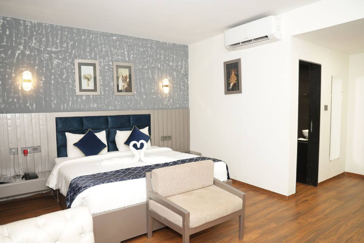 A hotel room with a bed, a chair, a nightstand, and a wall-mounted air conditioner.