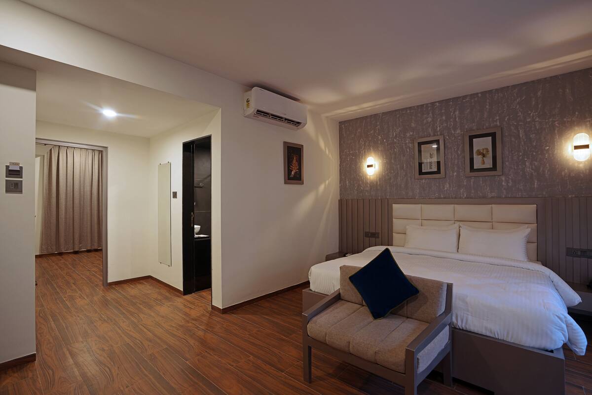 A hotel room with a large bed, a chair with a pillow, a mirror, and a wall-mounted air conditioner.