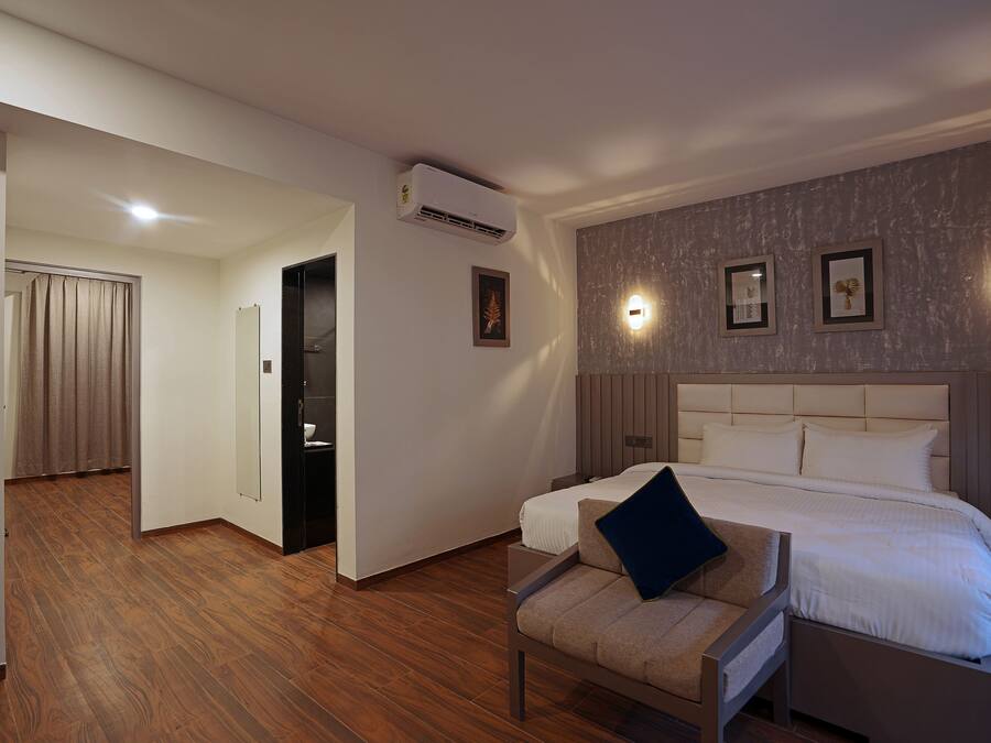 Habitación de hotel con una cama grande, una silla con cojín, un espejo y un aire acondicionado instalado en la pared.