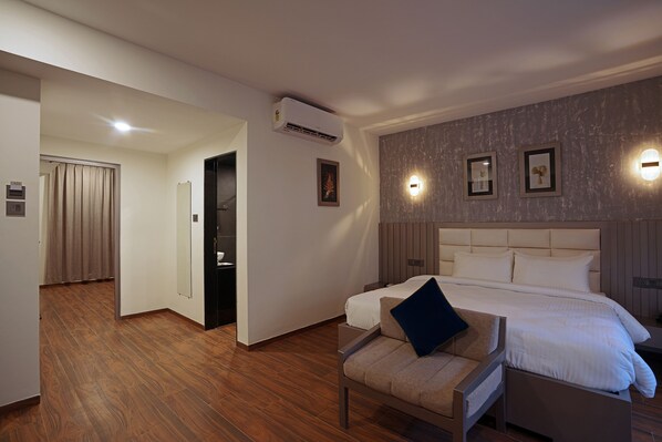 Habitación de hotel con una cama grande, una silla con cojín, un espejo y un aire acondicionado instalado en la pared.