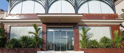 A modern building with a large glass entrance, brick facade, and decorative arches.