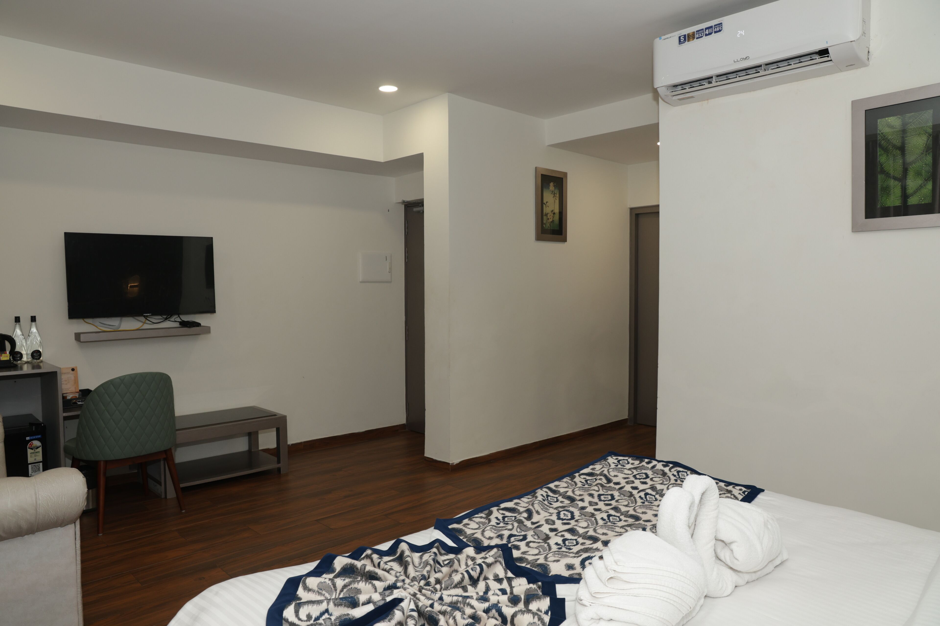 Una habitación de hotel con cama, escritorio con silla, televisión y aire acondicionado.