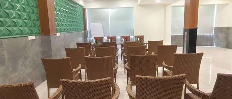 A spacious indoor area with rows of wicker chairs and tables, a whiteboard, and a green textured wall.