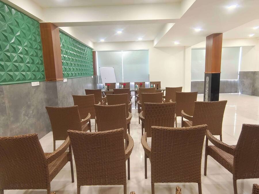 A spacious indoor area with rows of wicker chairs and tables, a whiteboard, and a green textured wall.