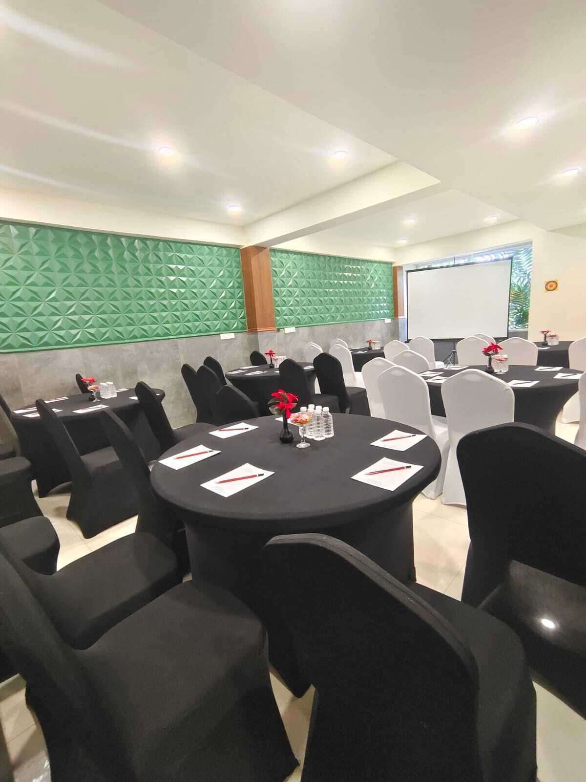 A conference room with round tables, black chairs, and a green textured wall.