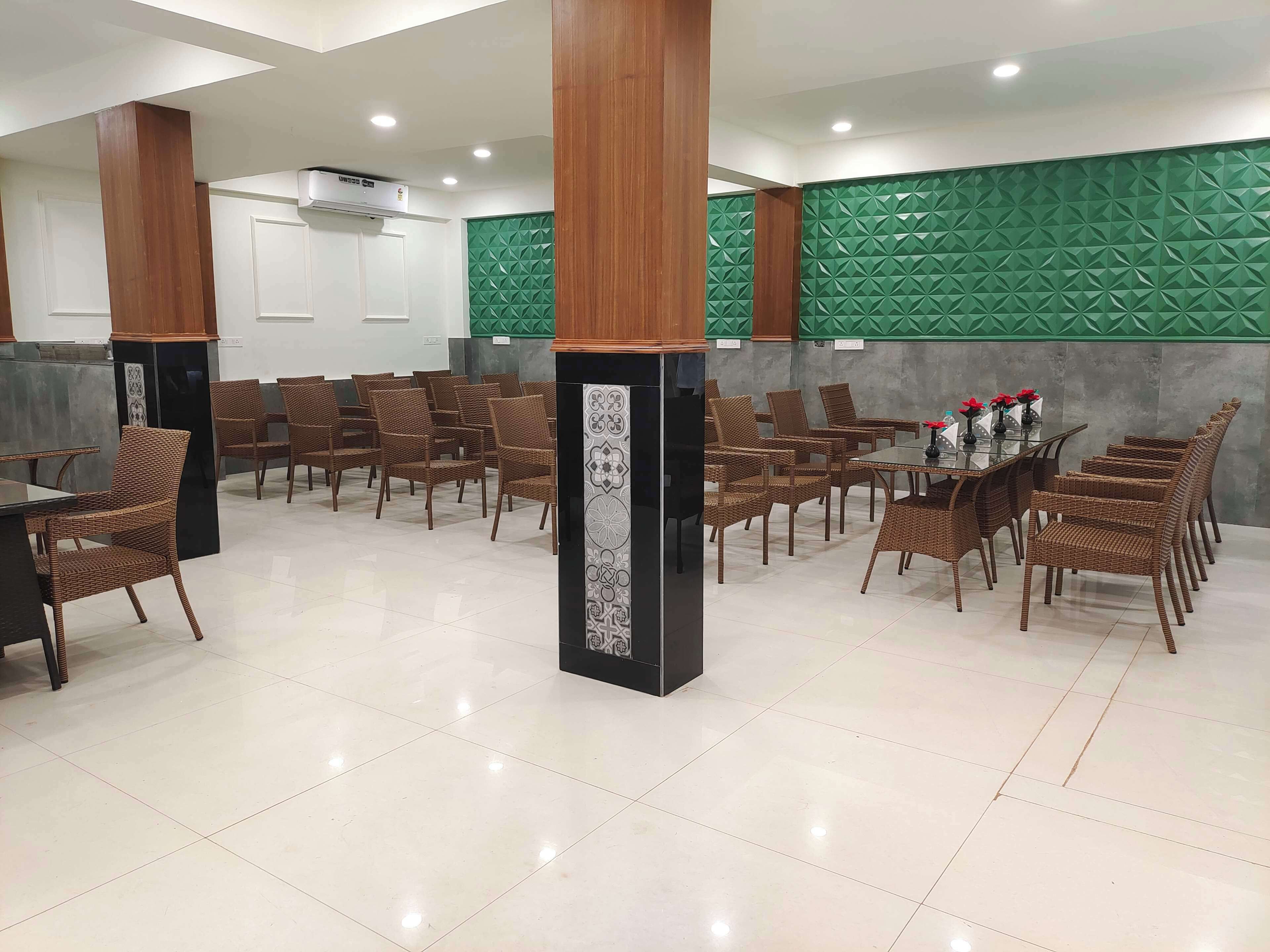 A spacious dining area with multiple tables and wicker chairs, featuring a green textured wall and a modern ceiling design.