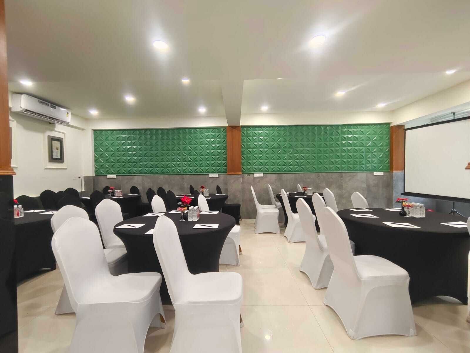 Un salón de conferencias con mesas redondas, sillas blancas y una pantalla de proyector.