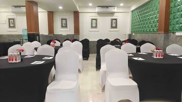 Un salón de conferencias con varias mesas, sillas blancas y manteles negros.