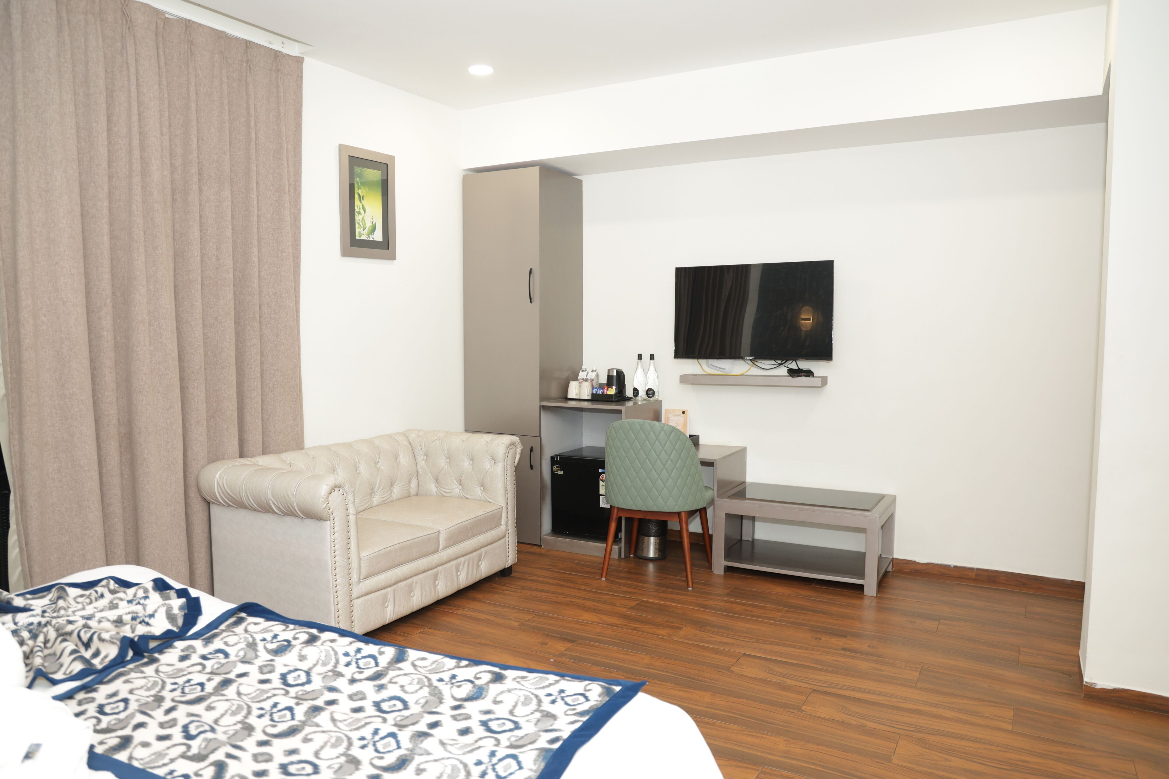 A hotel room with a bed, a sofa, a desk with a chair, a television, and a minibar.