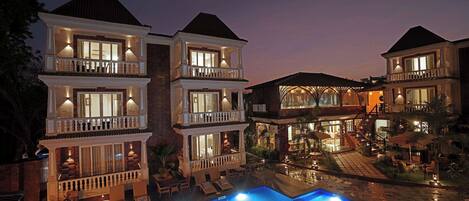 A multi-story hotel with a swimming pool, outdoor seating, and well-lit balconies.