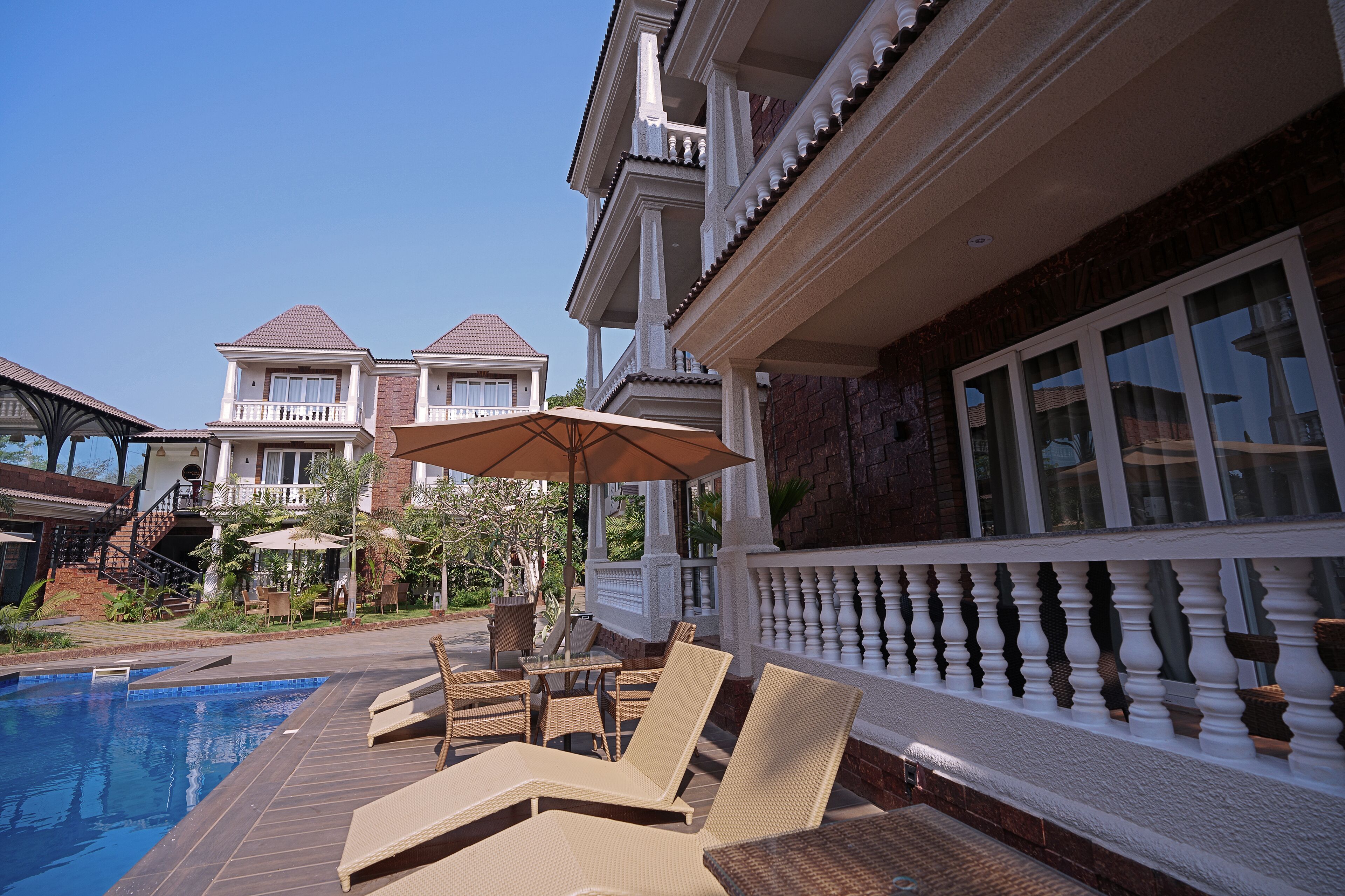A poolside area with lounge chairs and a table, surrounded by a white balustrade and a brick wall.