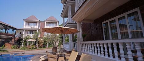 A poolside area with lounge chairs and a table, surrounded by a white balustrade and a brick wall.