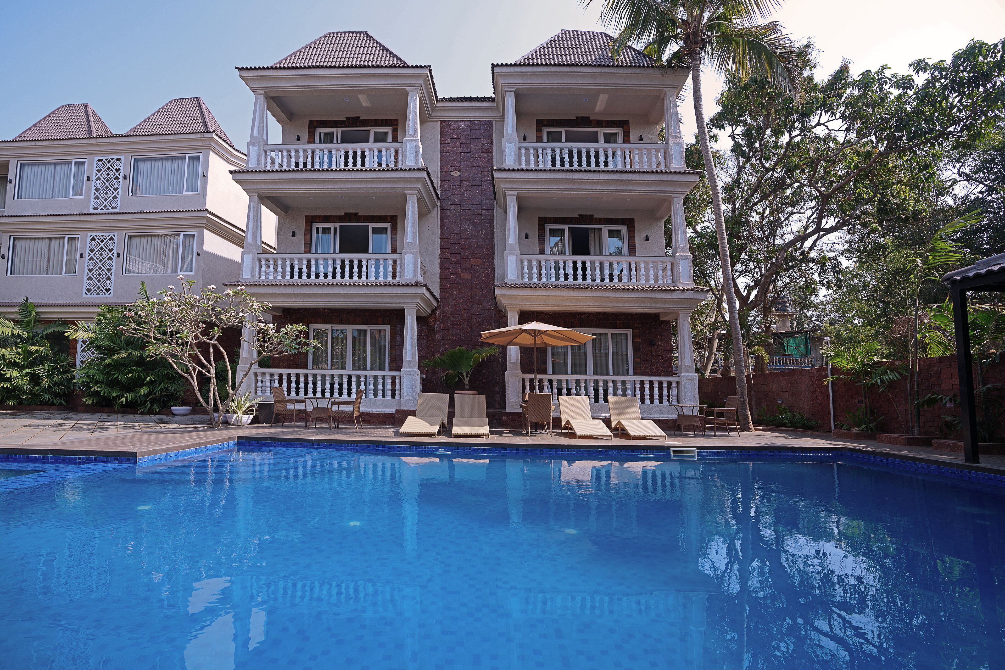A swimming pool with lounge chairs and umbrellas, surrounded by a multi-story building with balconies.