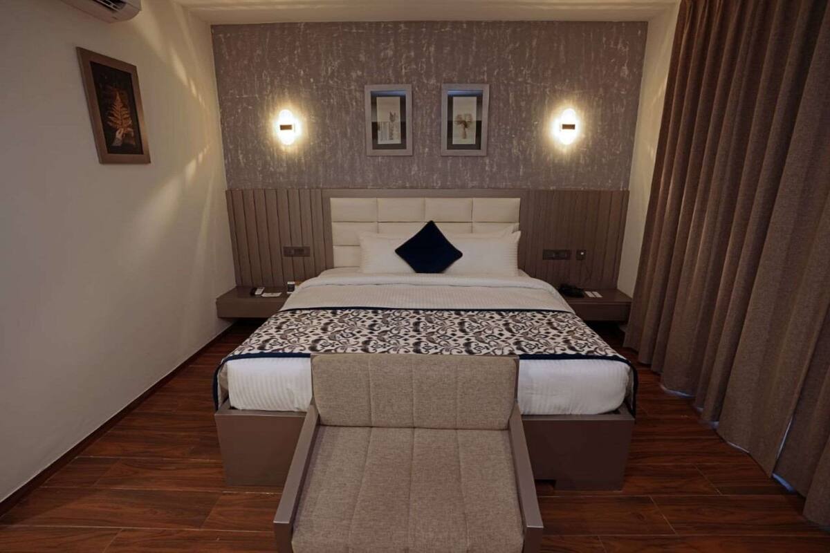 A modern hotel room with a large bed, a headboard with built-in lighting, a bedside table, and a nightstand.