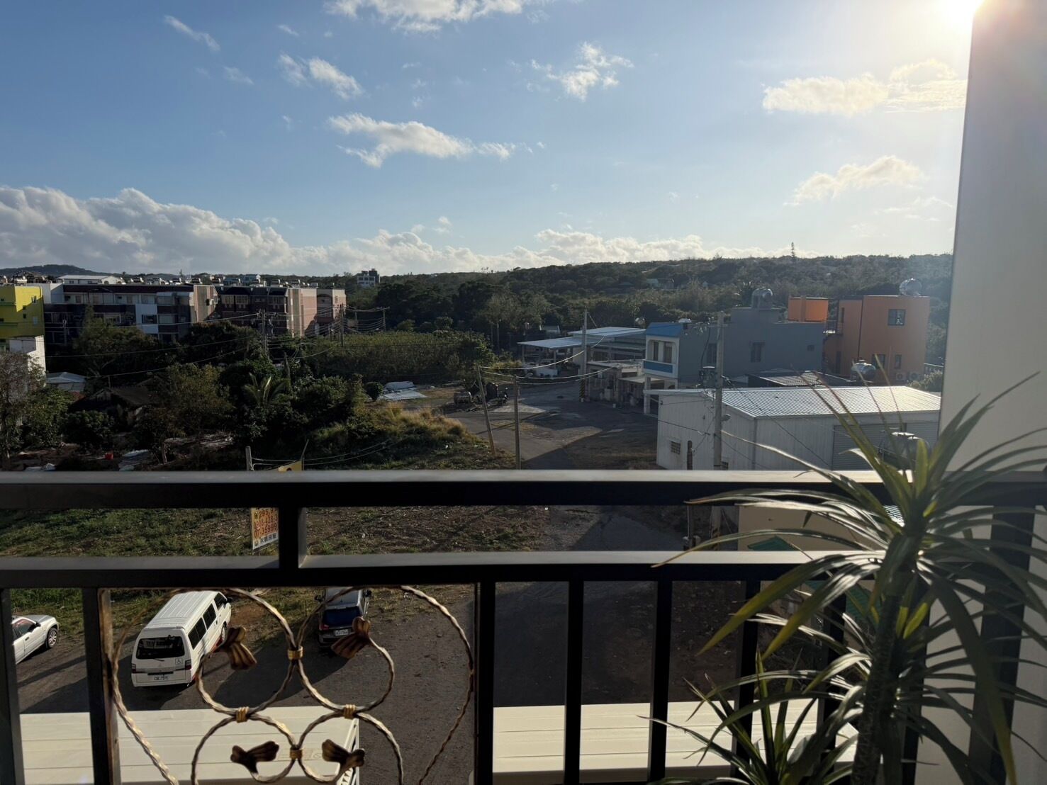 Un balcon donnant sur un parking, des immeubles et un ciel dégagé.