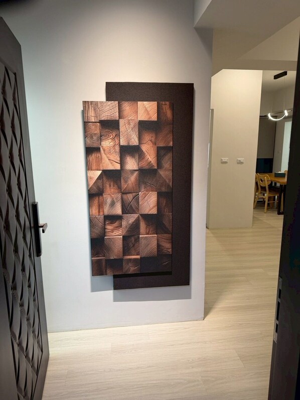 A hallway with a modern wall art piece and a dining area in the background.