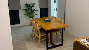 A modern dining area with a wooden table and chairs, a potted plant, and a ceiling light fixture. - Luxury Apartment (Hengchun)