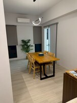A modern dining area with a wooden table and chairs, a potted plant, and a ceiling light fixture.