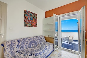 A room with a patterned sofa, a colorful abstract painting, a sliding glass door leading to a balcony with a view of the sea. - Penthouse Azzurra Sea View Near Beach (Morciano di Leuca)