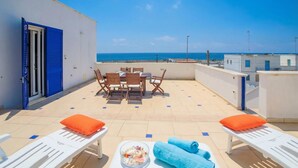A terrace with a table, chairs, and lounge chairs, overlooking the sea. - Penthouse Azzurra Sea View Near Beach (Morciano di Leuca)