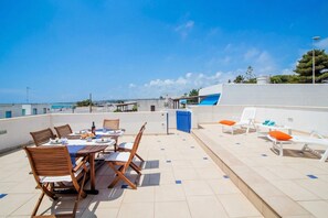 A rooftop terrace with a dining table set, chairs, and lounge chairs. - Penthouse Azzurra Sea View Near Beach (Morciano di Leuca)