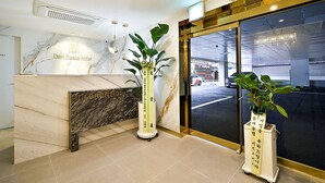 A hotel reception area with a marble counter, a reception desk, and potted plants. - Den Basta Hotel Daeyeon (Busan)