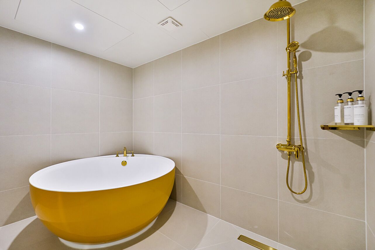 A bathroom with a yellow bathtub, a gold showerhead, and a shelf with toiletries.