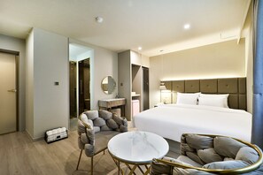 A hotel room with a large bed, a round marble table, two armchairs, a small round table, a mirror, and a bathroom visible through an open door. - Den Basta Hotel Daeyeon (Busan)