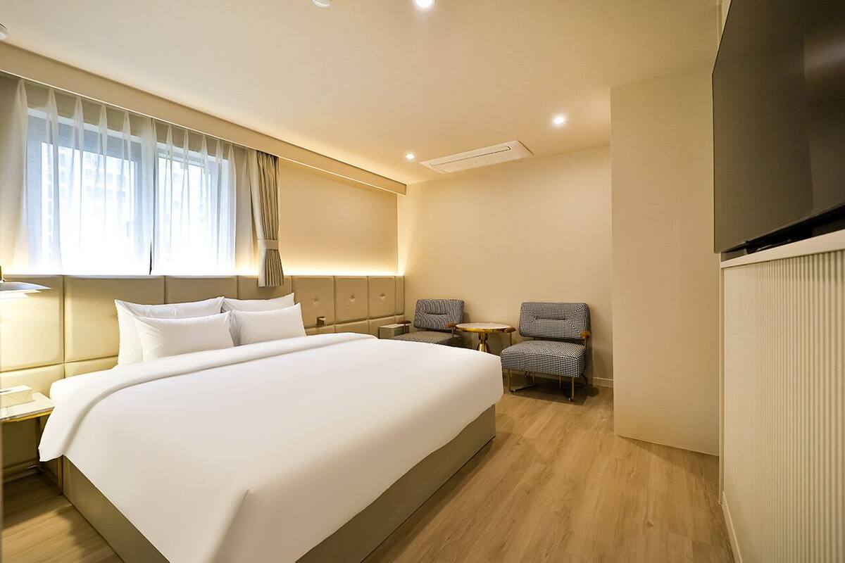 Una habitación de hotel con una cama grande, dos sillones, una mesita y un televisor.