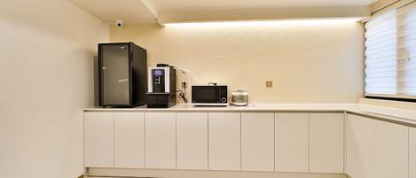 A compact kitchen with a refrigerator, microwave, and coffee maker on a white countertop.