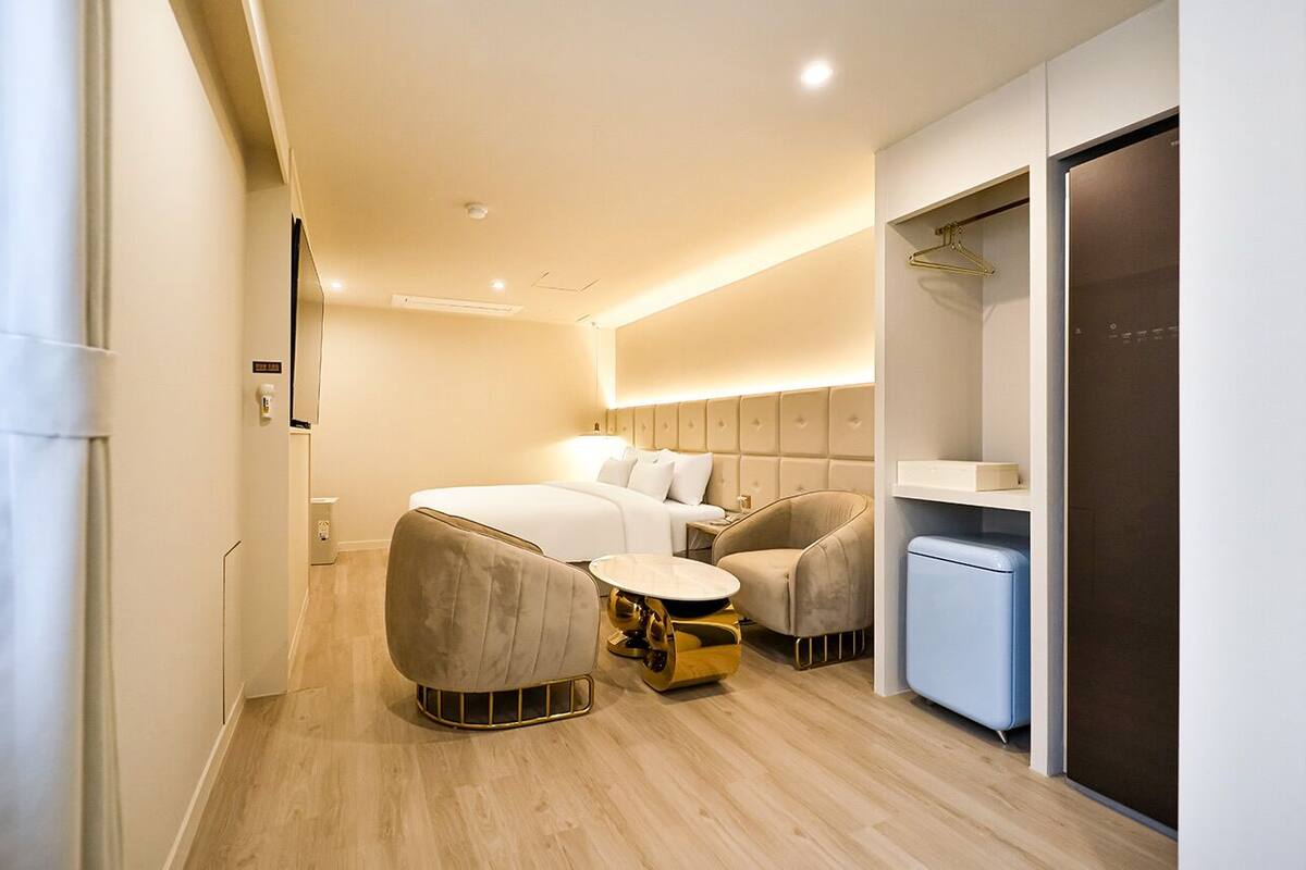 Una habitación de hotel moderna con cama, dos sillones, una mesita, minibar y armario.