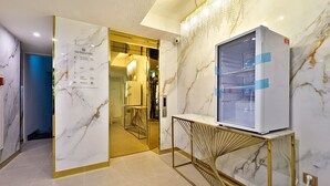A hotel lobby with marble walls, a reception desk, and a modern elevator. - Den Basta Hotel Daeyeon (Busan)