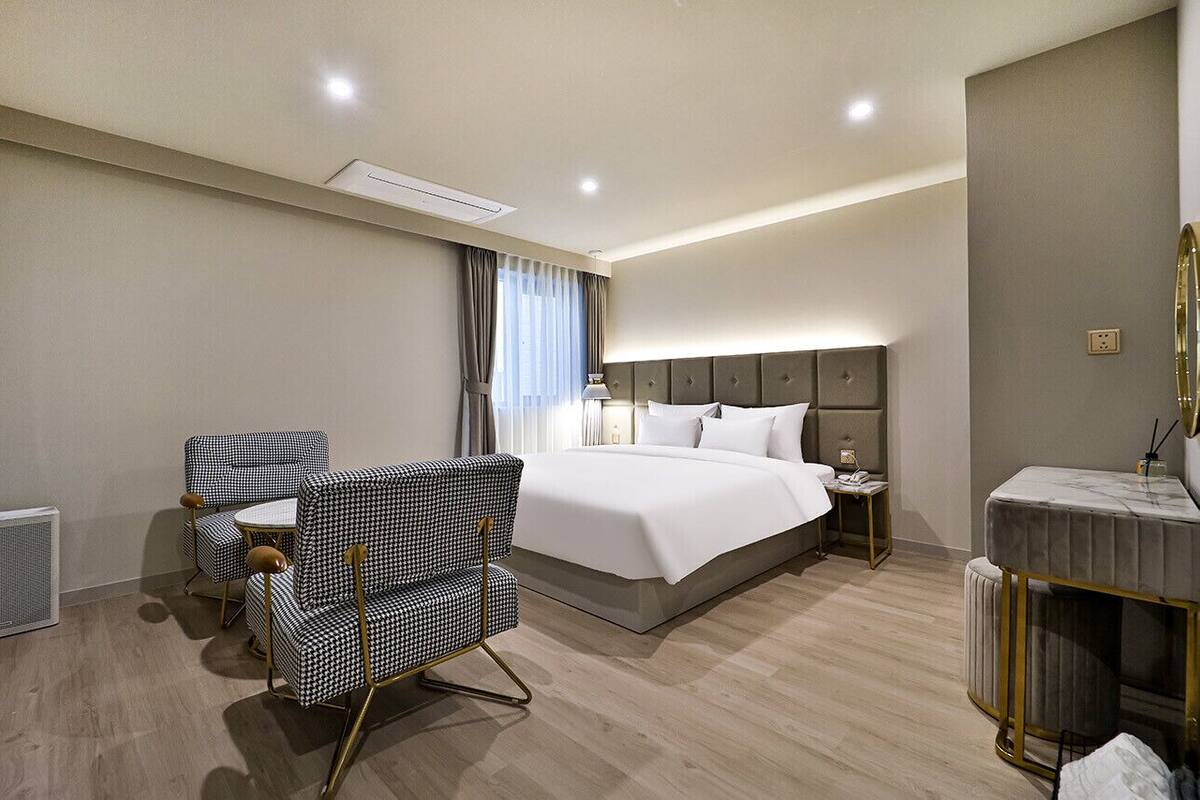 Una habitación de hotel con una cama grande, una silla, una mesita y un escritorio con una lámpara.