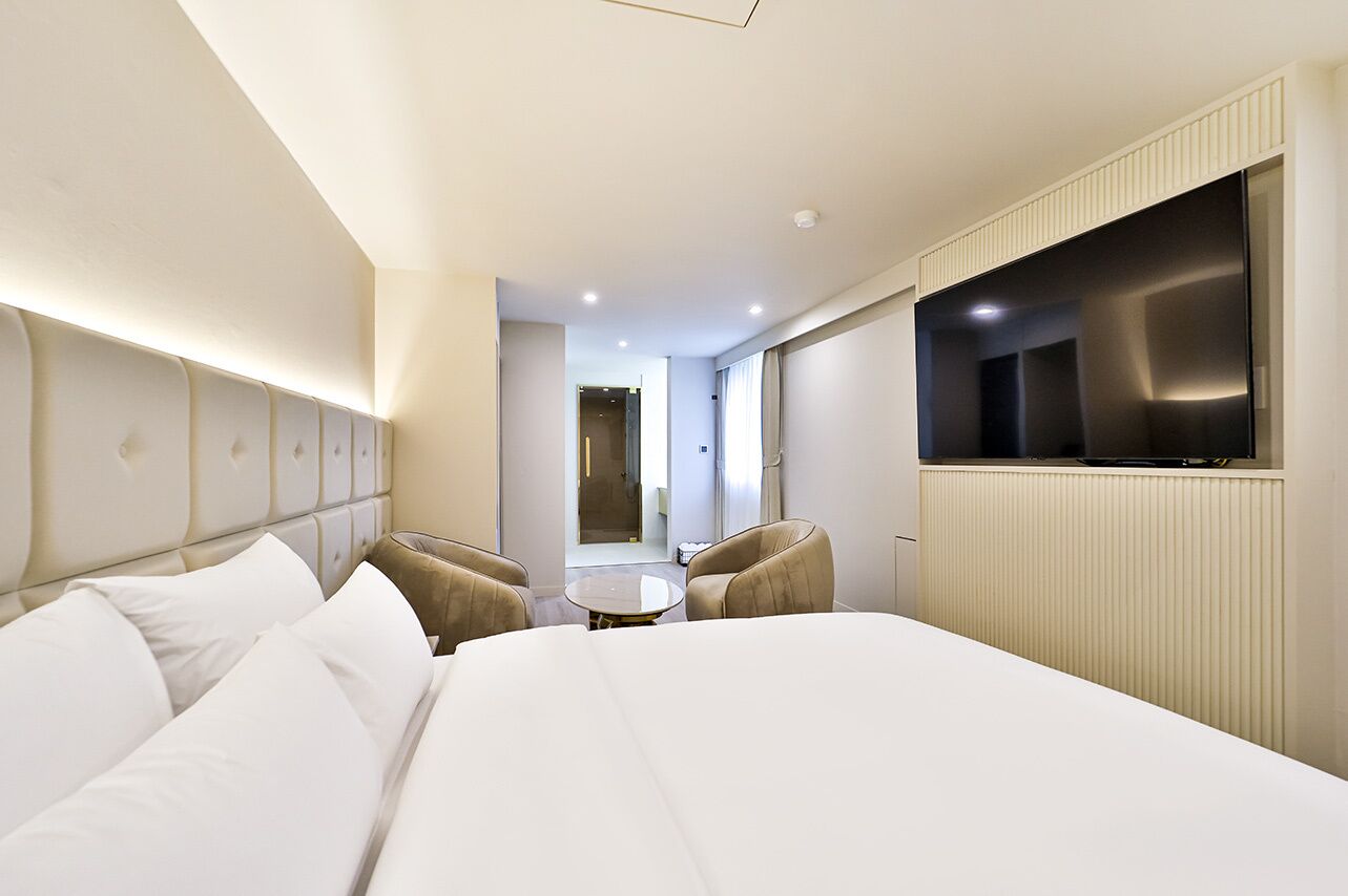 A hotel room with a large bed, a TV mounted on the wall, a small table, and two chairs.