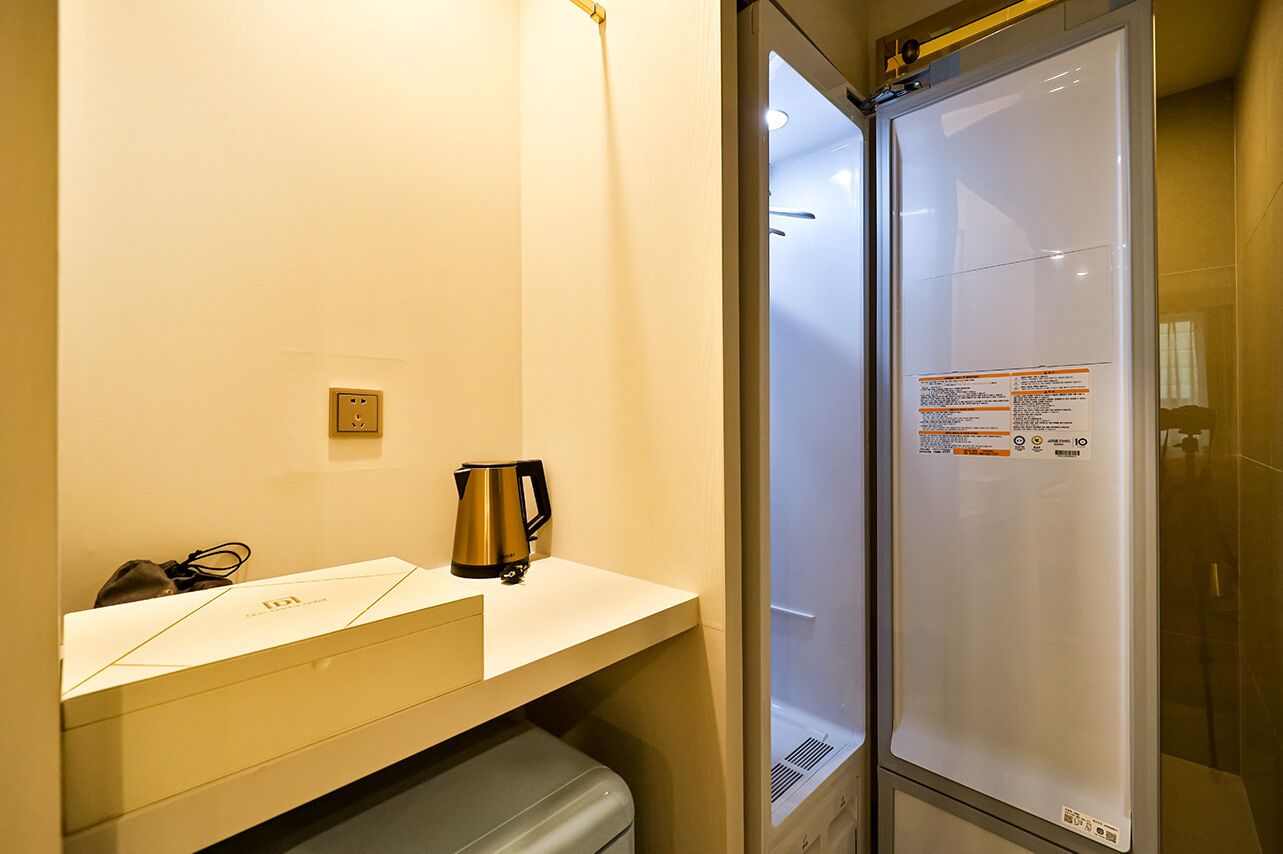 Een hotelkamer met een minibar, een waterkoker en een douchecabine van glas.