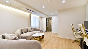 A modern hotel room with a sofa, a round coffee table, a desk with a chair, and a television. - Den Basta Hotel Daeyeon (Busan)