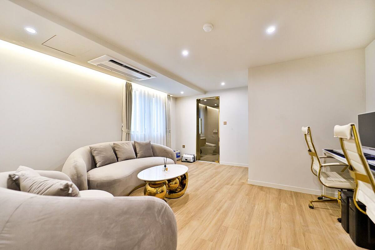 Una habitación de hotel moderna con un sofá, una mesa redonda de centro, un escritorio con una silla y un televisor.