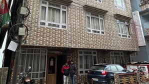 A multi-story building with a checkered pavement in front, a parked motorcycle, and a car. - Hotel Highland Unit Of Vaishnavi Hotels (Gangtok)