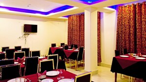 A dining area with tables set for a meal, featuring red tablecloths and patterned curtains. - Hotel Highland Unit Of Vaishnavi Hotels (Gangtok)
