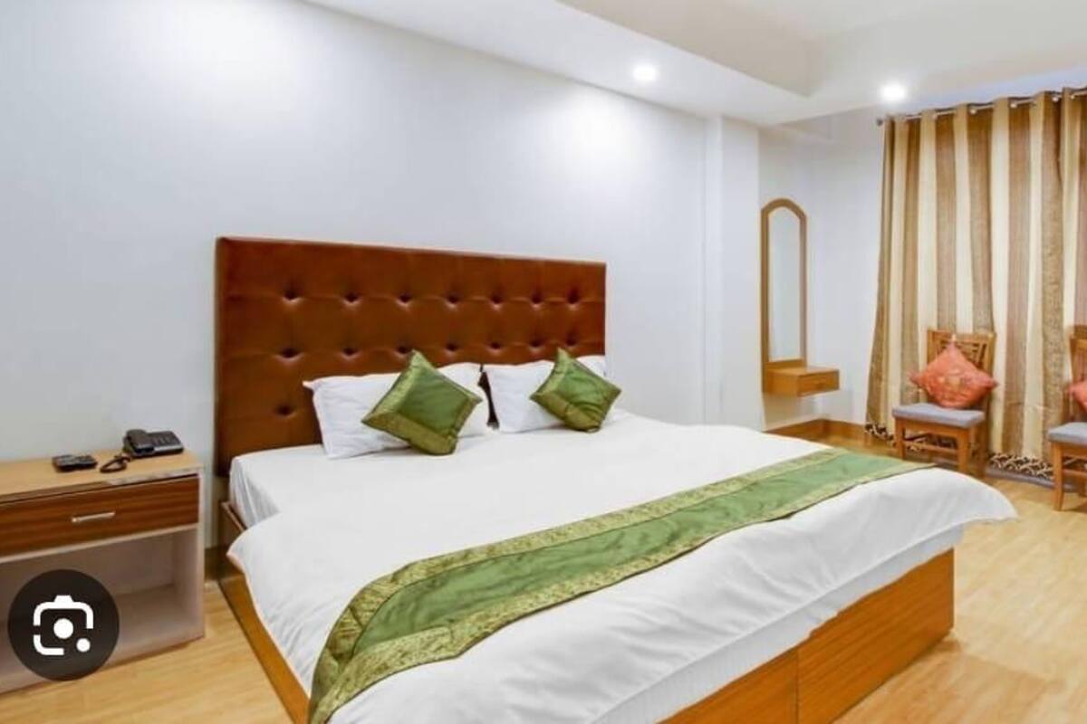 A hotel room with a large bed, a nightstand, a mirror, two chairs, and a curtain.