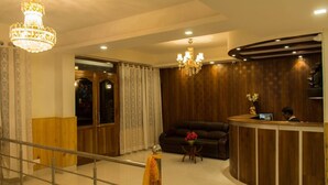 A hotel lobby with a reception desk, a sofa, a chandelier, and a wooden wall. - Hotel Highland Unit Of Vaishnavi Hotels (Gangtok)