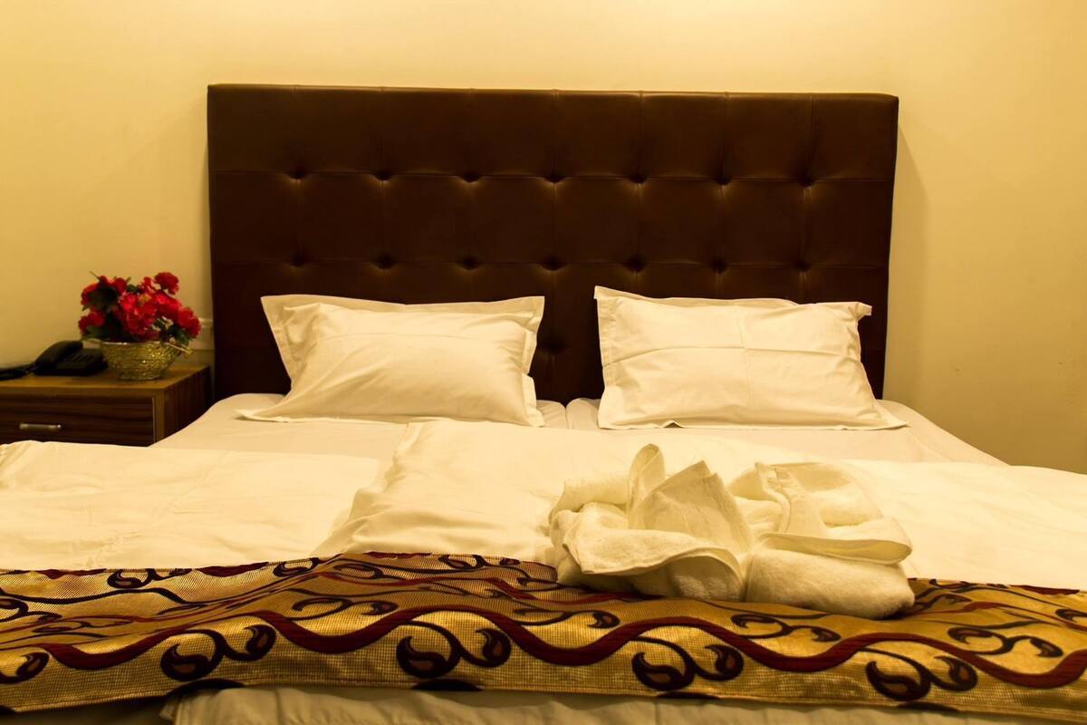 A neatly made bed with white linens and two pillows, a dark headboard, and a decorative throw blanket with a gold and red pattern.