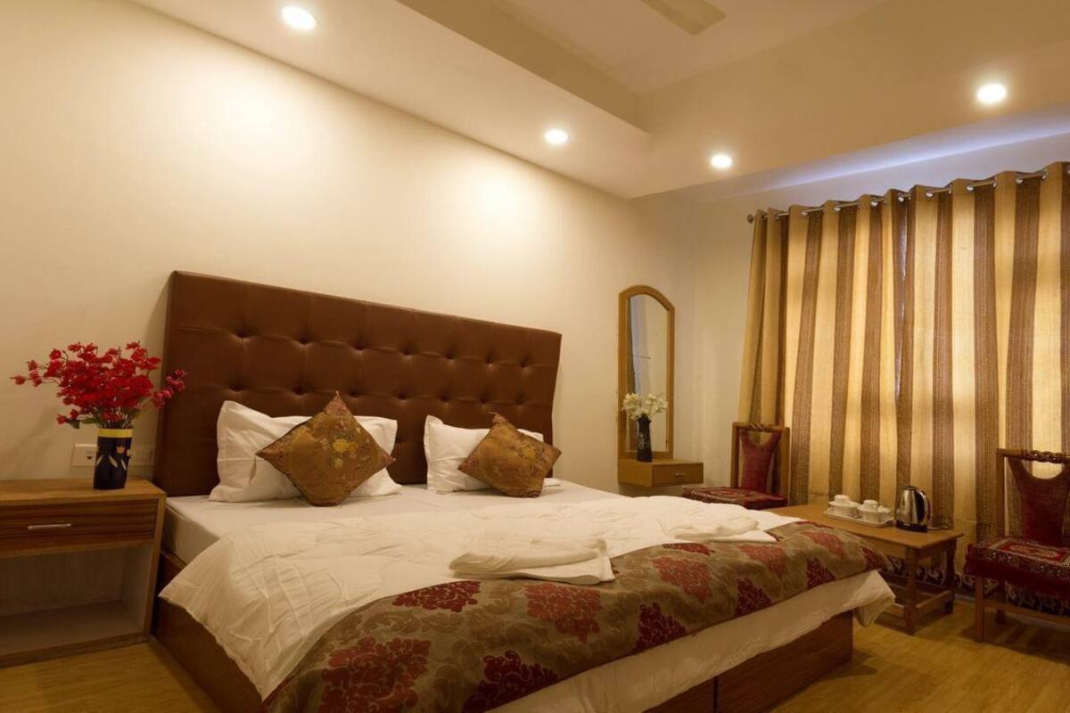 A well-lit bedroom with a large bed, a nightstand, a chair, a mirror, and a curtain.