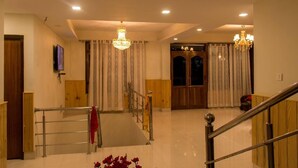 A spacious lobby with a grand staircase, chandeliers, and a wooden door. - Hotel Highland Unit Of Vaishnavi Hotels (Gangtok)