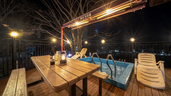 A wooden deck with a pool, lounge chairs, and a table with a bottle and glass. - Boryeong Thirasel Pension (Boryeong)