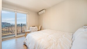 A bedroom with a large bed, a small table, a chair, and a view of the beach through a sliding door. - Boryeong Thirasel Pension (Boryeong)