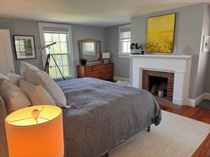 Un dormitorio con una cama grande, chimenea, cómoda y espejo.