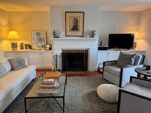 A living room with a fireplace, sofa, armchair, coffee table, and television.