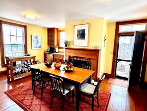 Un comedor con mesa de madera, sillas, frutero y chimenea.