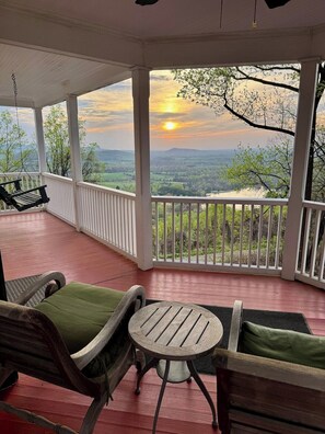 A covered porch with a swing chair, a table, and chairs with cushions.